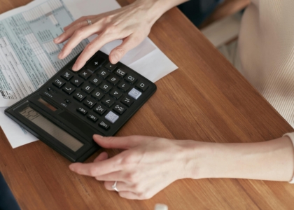 Een hand gebruikt een rekenmachine boven papieren documenten.
